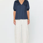 Woman wearing a navy blue blouse and white pants on a white background