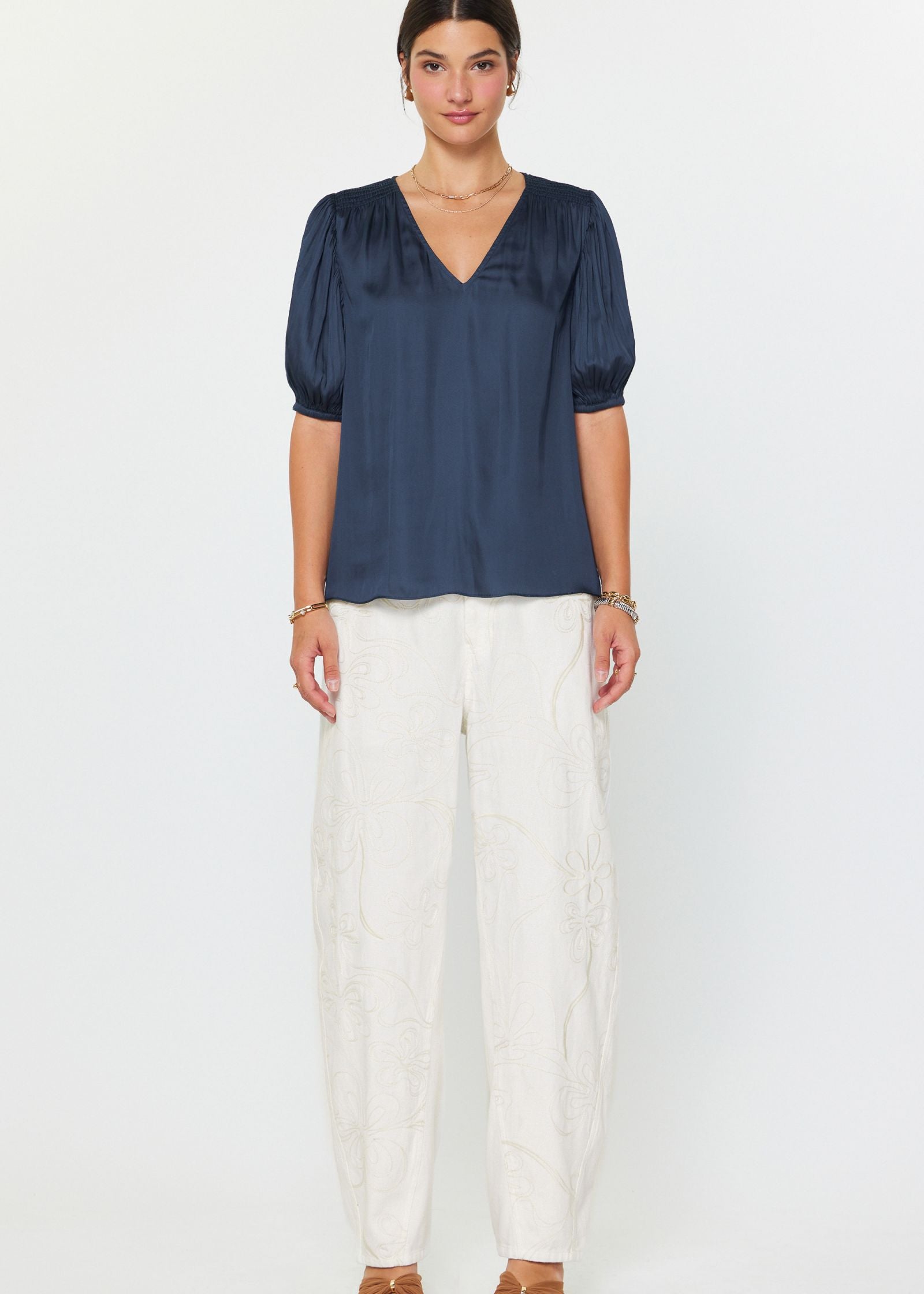 Woman wearing a navy blue blouse and white pants on a white background