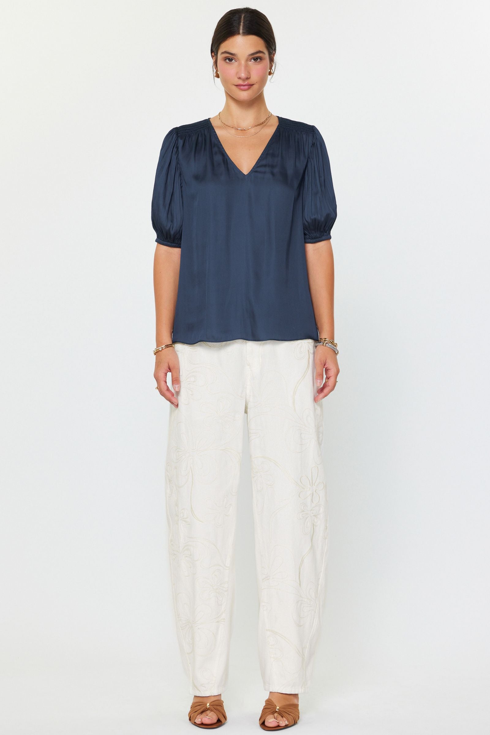 Woman wearing a navy blue blouse and white pants on a white background