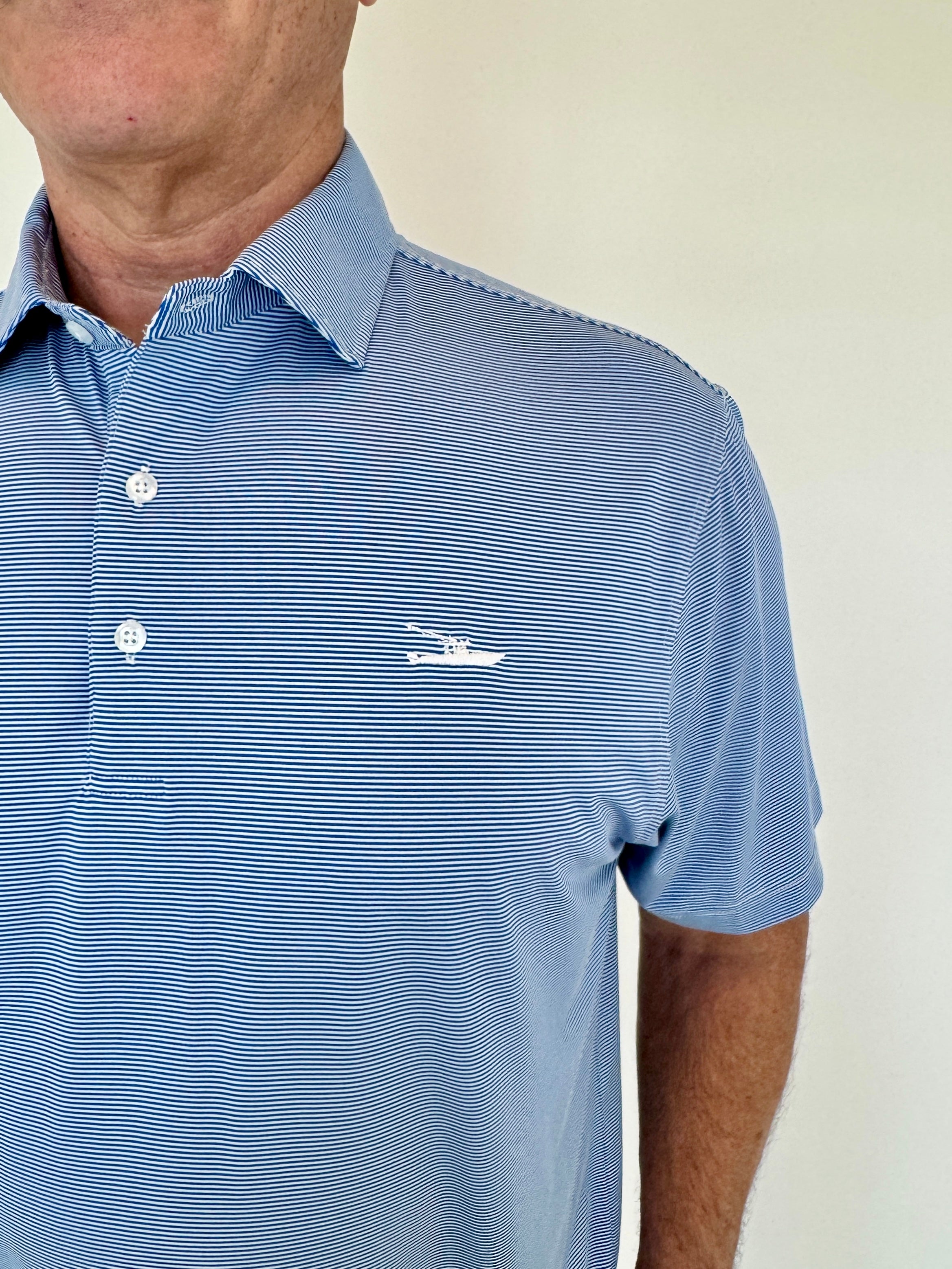 Man wearing a blue striped polo shirt with a logo on a plain background