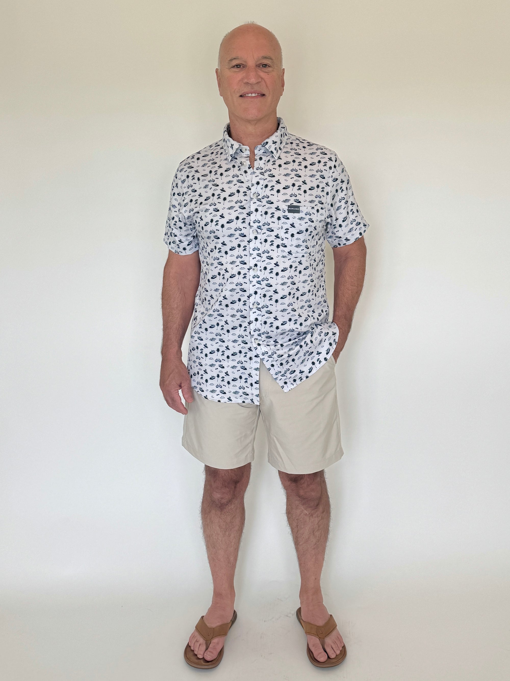 Man wearing a patterned shirt and beige shorts against a white background