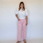Woman wearing a white blouse and pink wide leg ankle crop jeans  against a plain background
