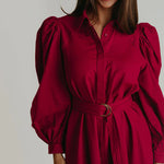 A woman wearing a Berry colored colored maxi dress with puffy long sleeves.