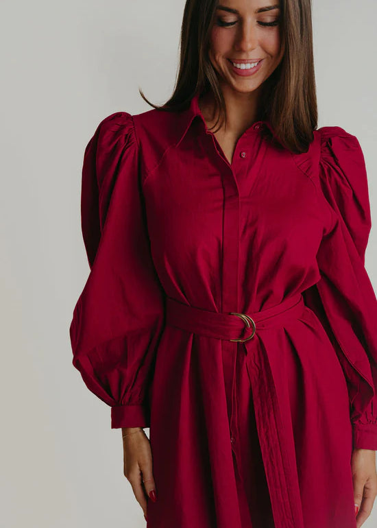 A woman wearing a Berry colored colored maxi dress with puffy long sleeves.