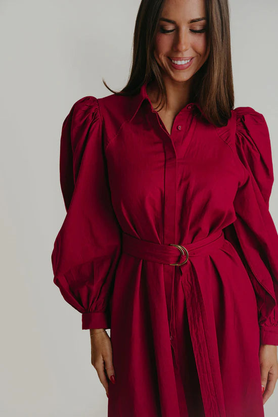 A woman wearing a Berry colored colored maxi dress with puffy long sleeves.