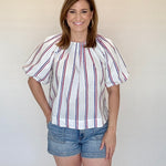 Woman wearing a striped blouse and denim shorts against a plain background