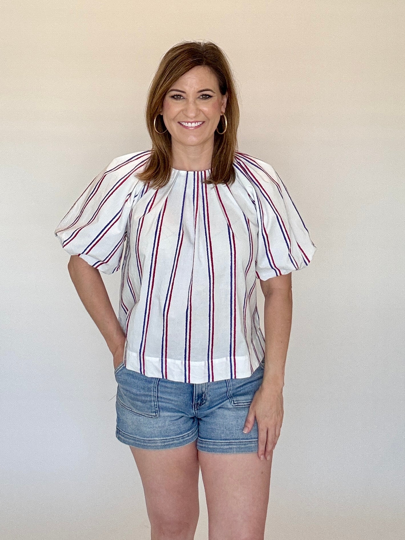 Woman wearing a striped blouse and denim shorts against a plain background