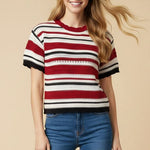 Woman wearing a red, white, and navy striped sweater with blue jeans on a beige background