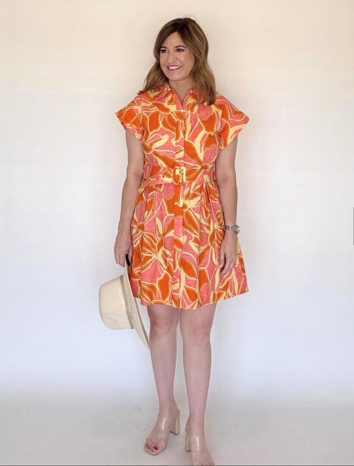 A woman wearing an orange, pink and yellow floral mini shirtdress with a collar and a belt.