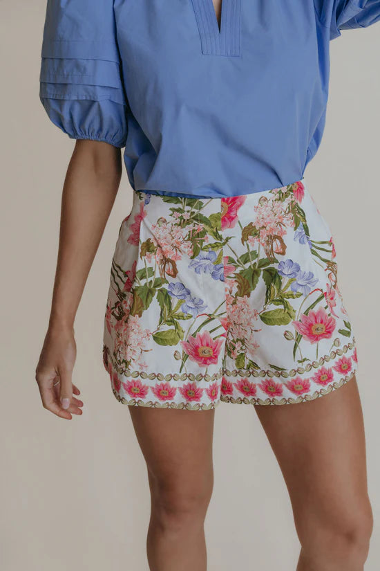 a woman wearing white dressy shorts with blue and pink florals.
