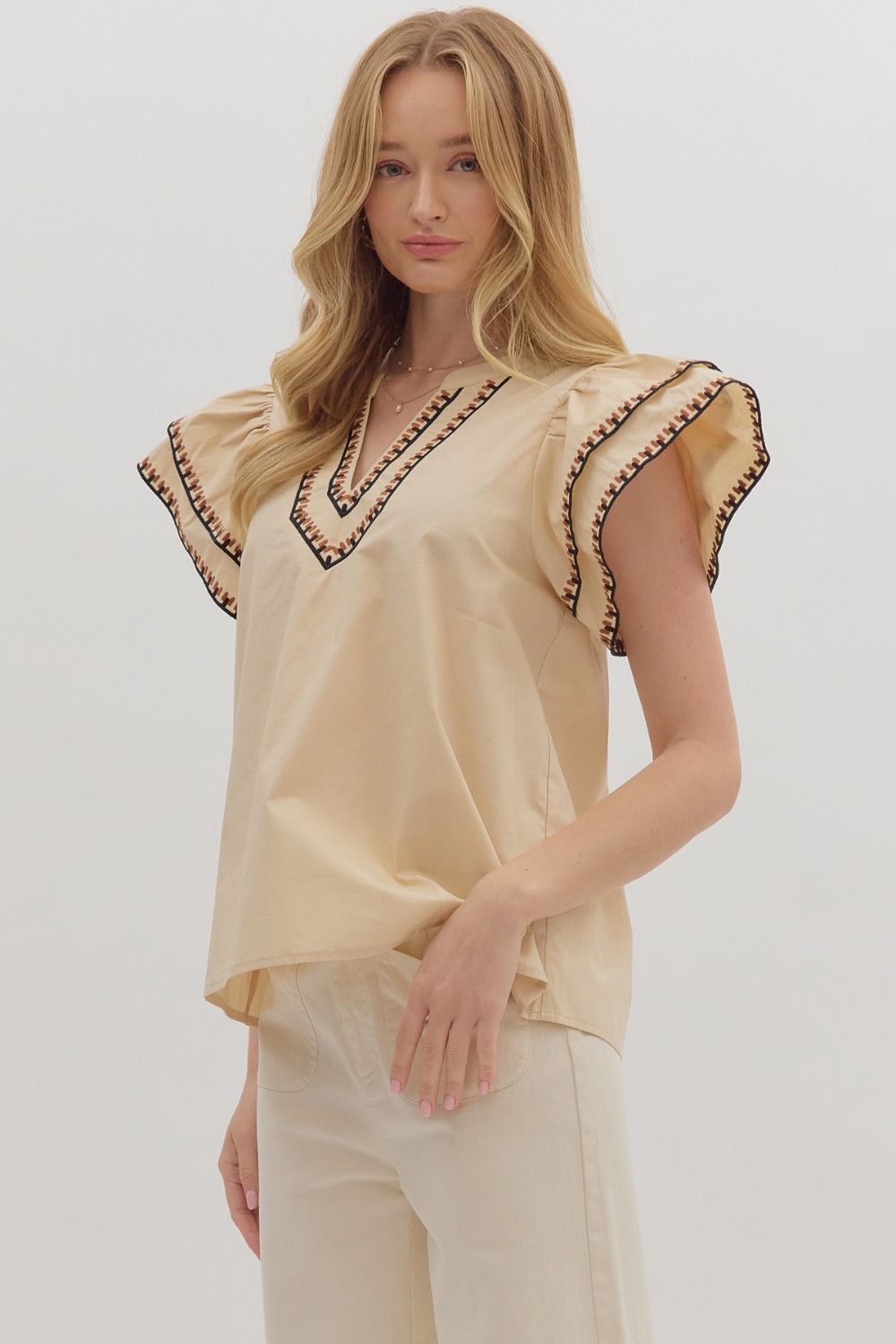 Woman wearing a beige blouse with decorative trim on a white background
