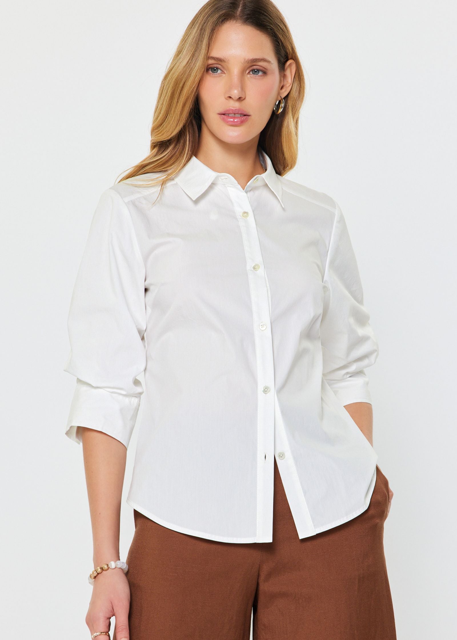 A woman wearing a white collared button down blouse with 3/4 sleeves.