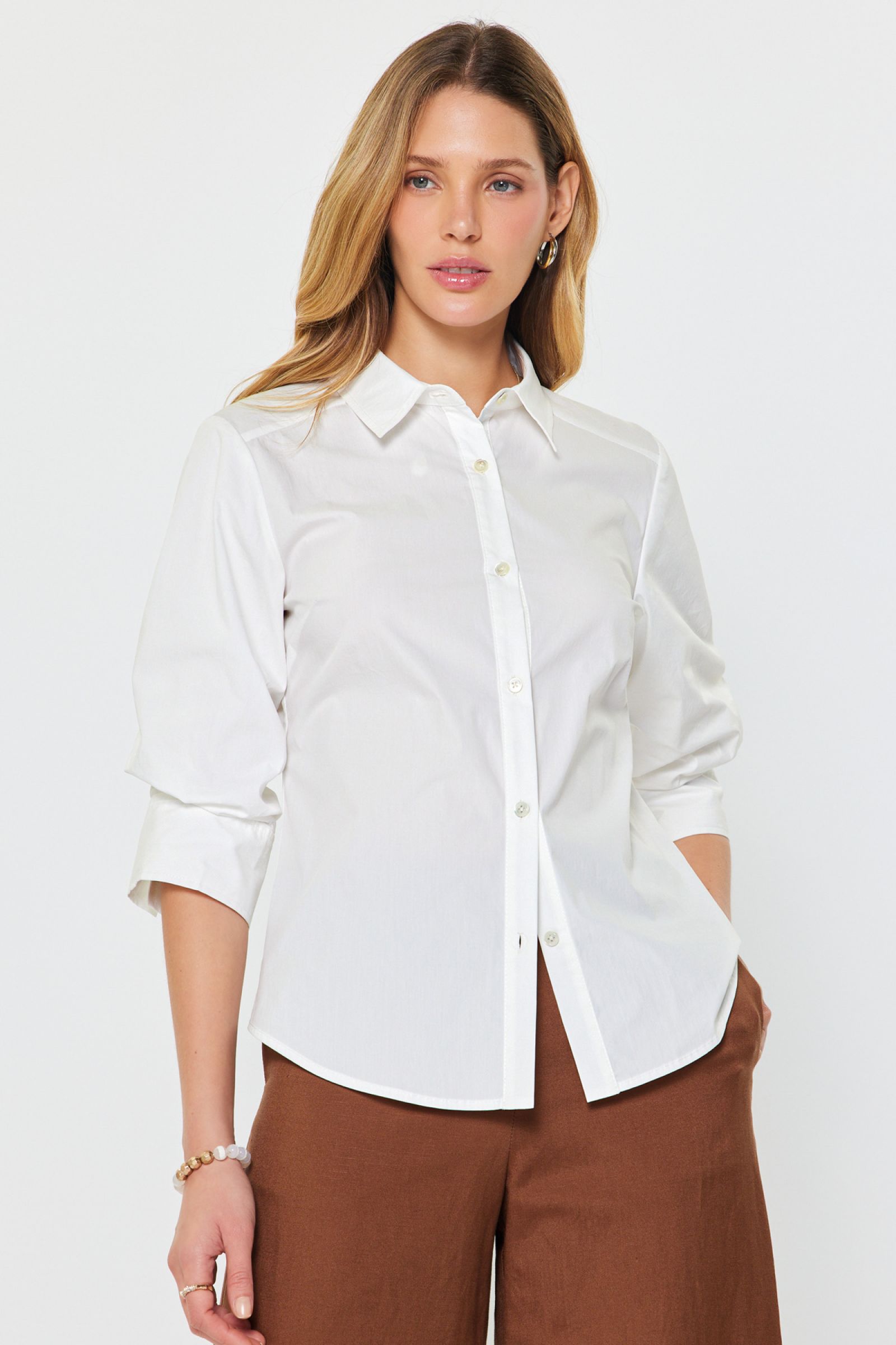 A woman wearing a white collared button down blouse with 3/4 sleeves.