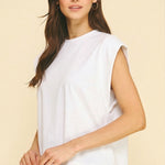 Woman wearing a white sleeveless top against a beige background