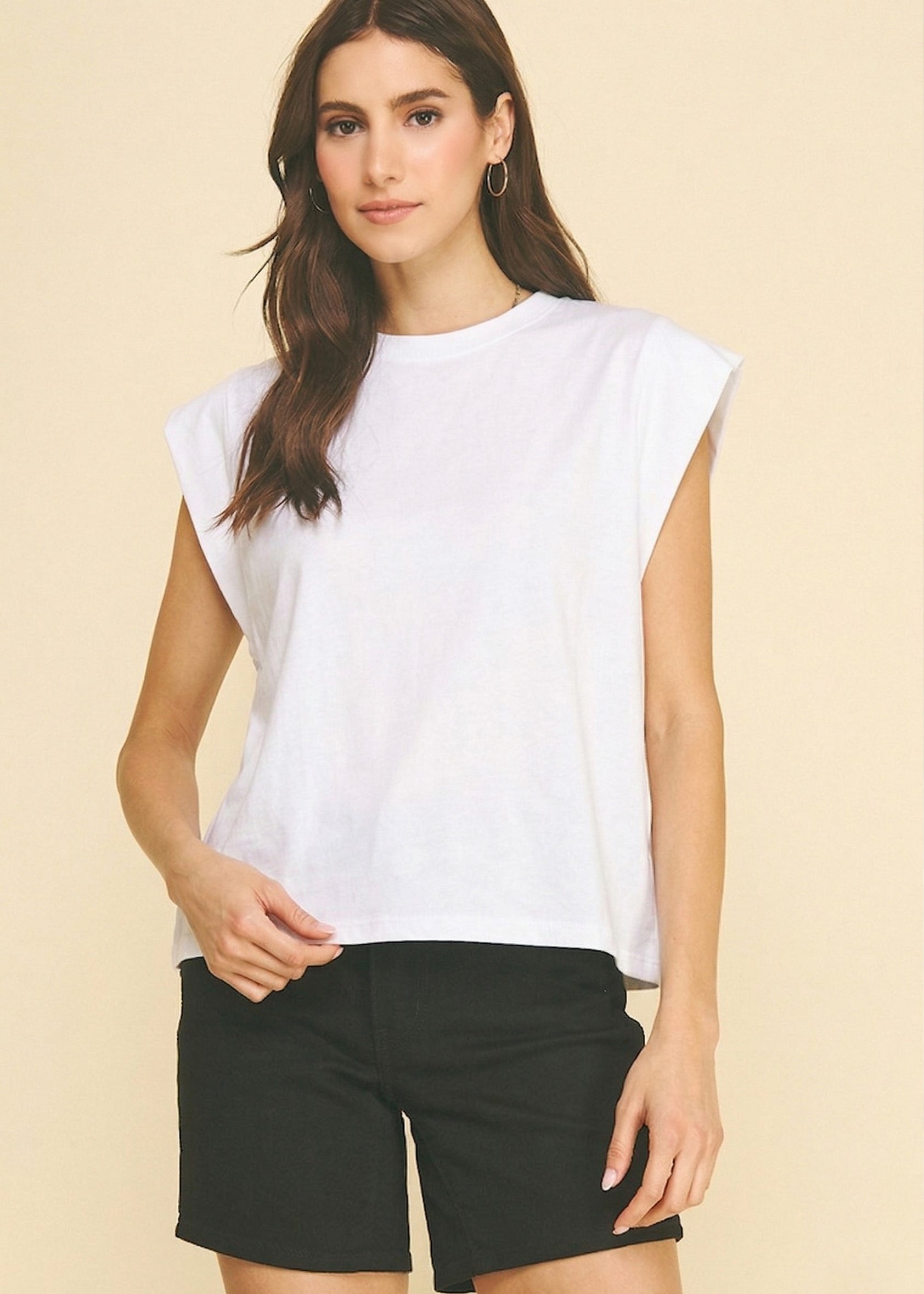 Woman wearing a white sleeveless top and black shorts on a beige background