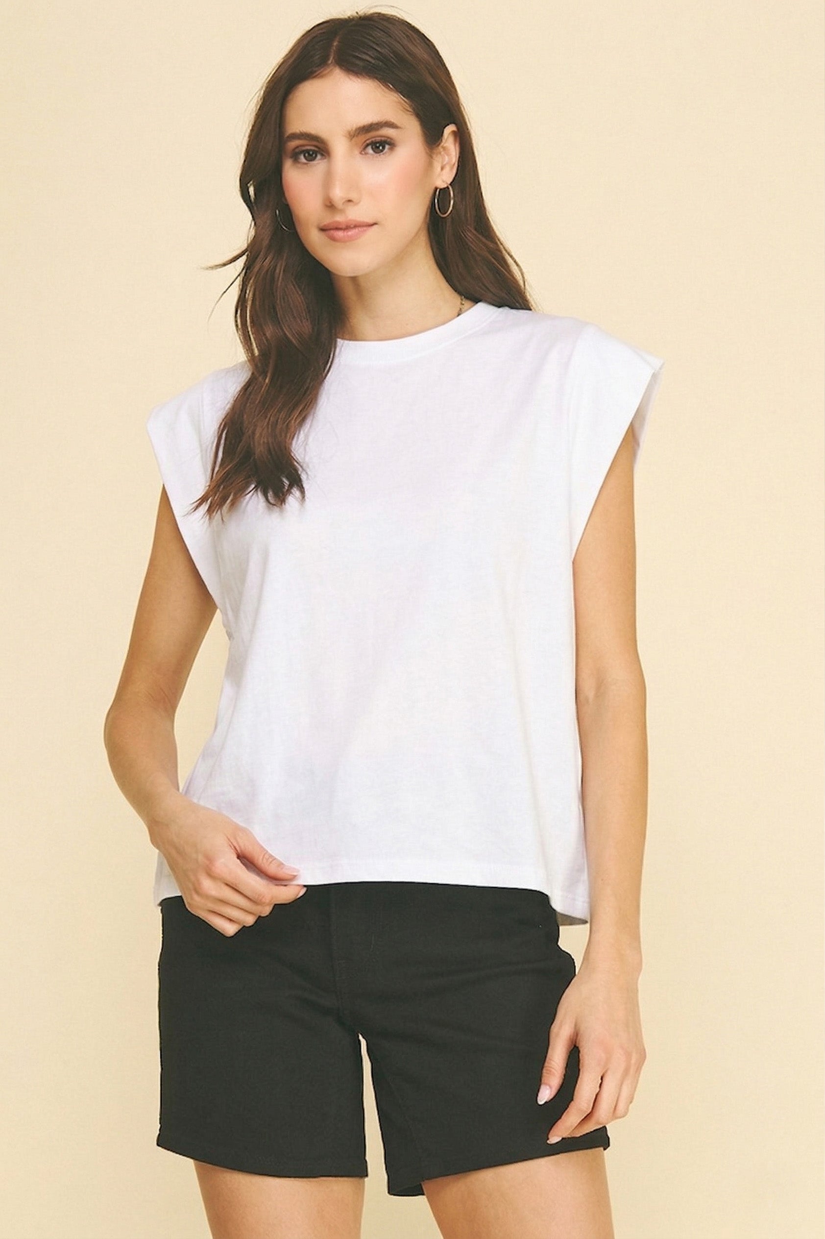 Woman wearing a white sleeveless top and black shorts on a beige background