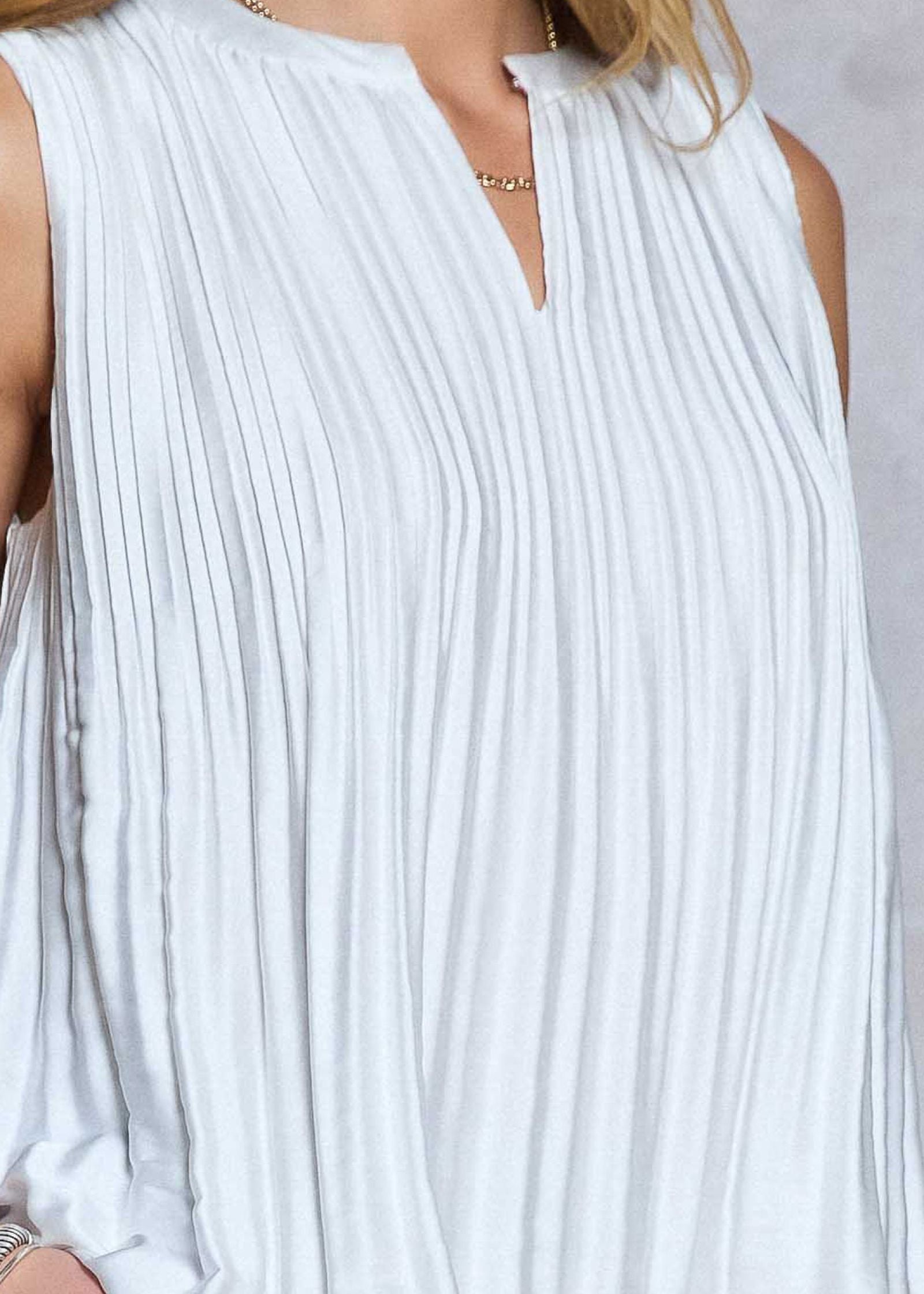 White pleated sleeveless top worn by a person on a light gray background