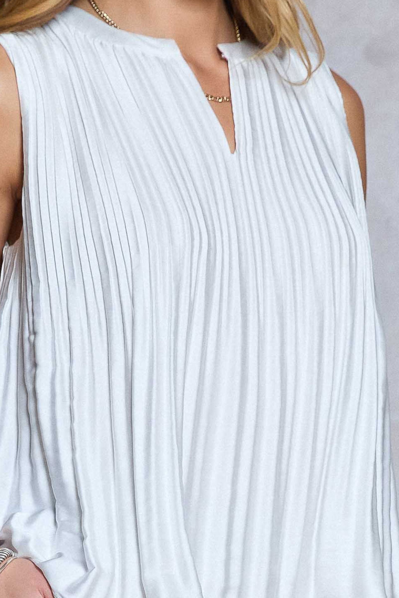 White pleated sleeveless top worn by a person on a light gray background