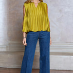 Woman wearing a yellow top and blue jeans against a neutral wall.
