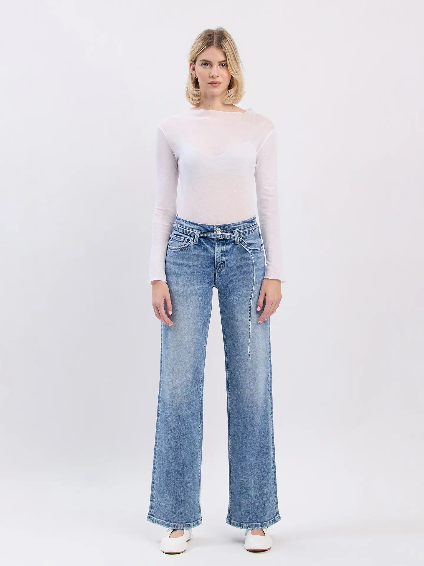 Woman wearing light blue jeans and a white top on a plain background