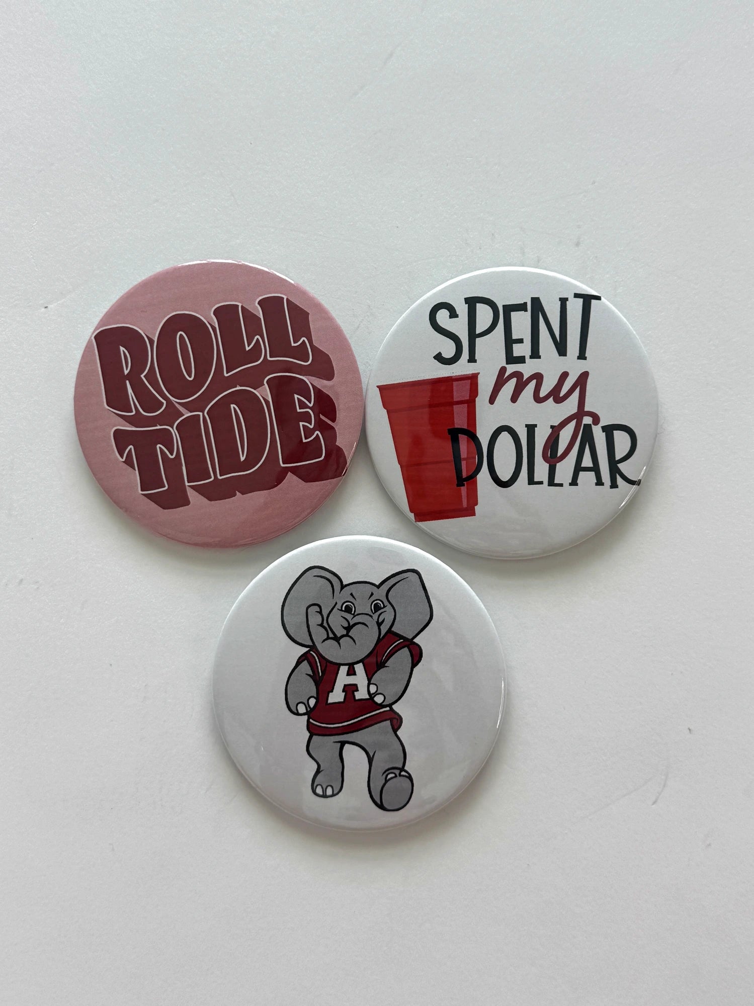 Alabama game day pin-back button set featuring Roll Tide, Spent My Dollar, and Elephant Mascot designs, from Chatsworth Boutique in Fairhope, Alabama.