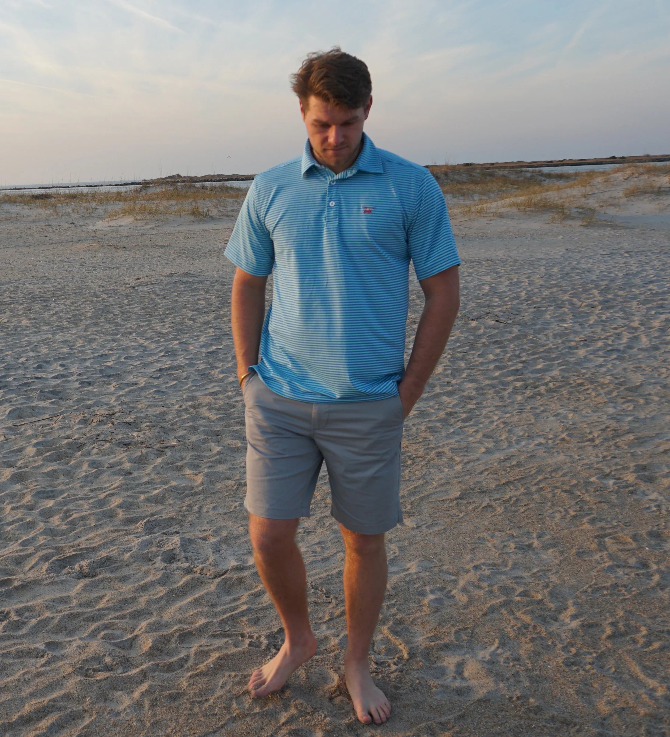 A man modeling the Albatross Performance Golf Polo in Aruba/Regatta Stripe by Bald Head Blues, styled with casual pants, from Chatsworth Boutique.
