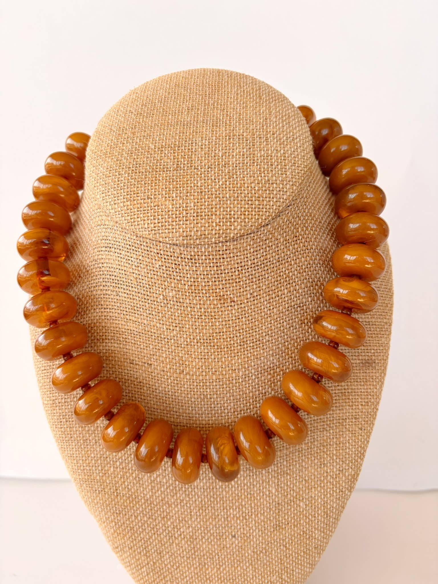 Brown beaded necklace on a beige mannequin head against a white background