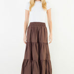 A model wearing the Chocolate Tiered Midi Skirt by THML, a cotton tiered midi skirt in chocolate, from Chatsworth Boutique in Fairhope, Alabama.