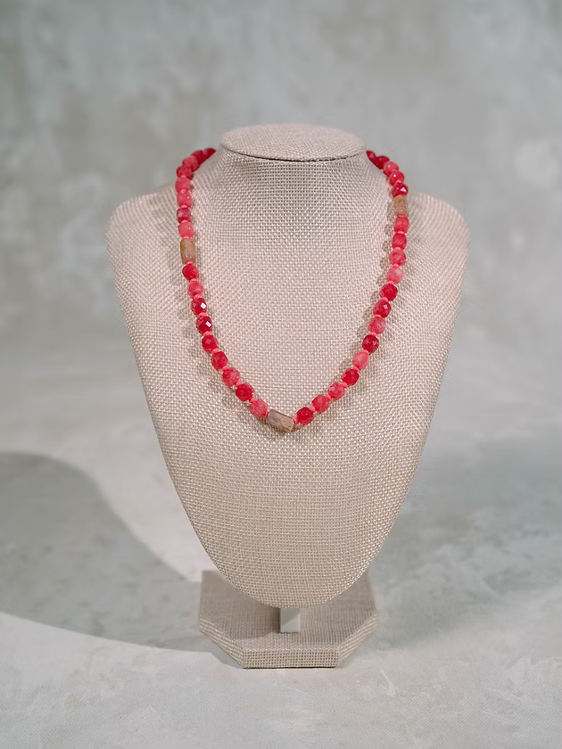 Necklace with red beads on a beige mannequin bust against a gray background