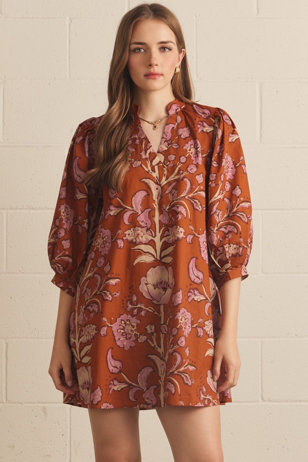 A model wearing the Floral V-Neck Mini in rust by Entro, a puff-sleeve mini dress with a V-neck collar, from Chatsworth Boutique in Fairhope, Alabama.