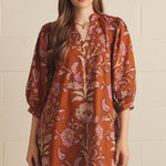 A model wearing the Floral V-Neck Mini in rust by Entro, a puff-sleeve mini dress with a V-neck collar, from Chatsworth Boutique in Fairhope, Alabama.