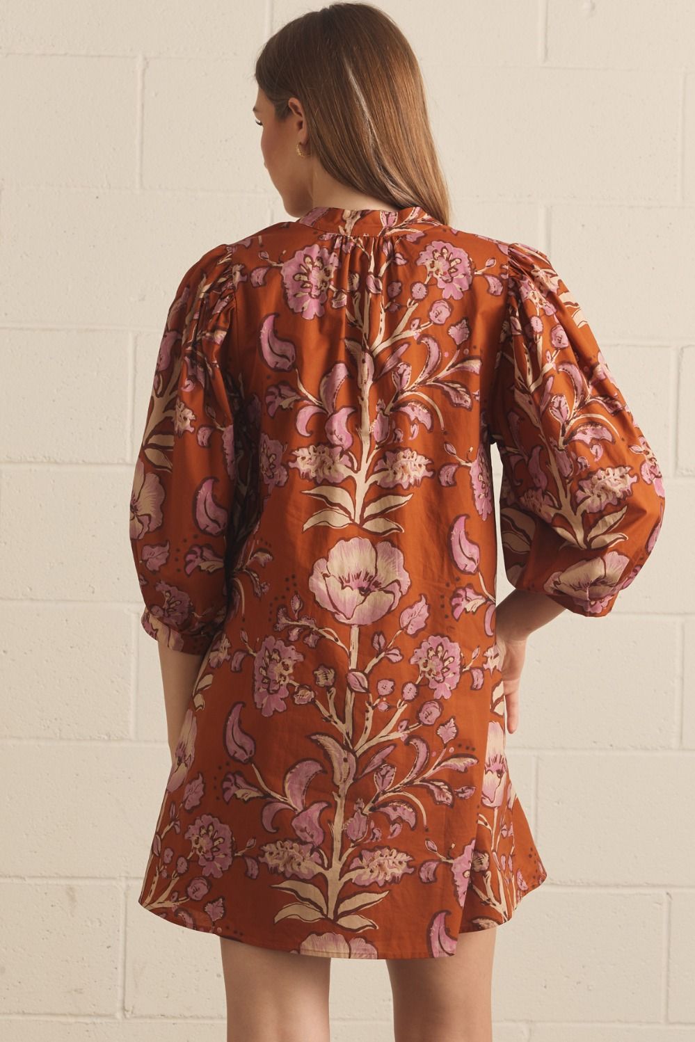 A model posing in the Floral V-Neck Mini in rust by Entro, a lightweight floral mini dress with side pockets, from Chatsworth Boutique in Fairhope, Alabama.