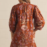 A model posing in the Floral V-Neck Mini in rust by Entro, a lightweight floral mini dress with side pockets, from Chatsworth Boutique in Fairhope, Alabama.