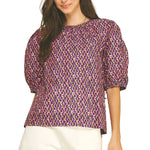 A model wearing the Geometric Print Puff Sleeve Blouse in navy and pink by PINCH, paired with white shorts, from Chatsworth Boutique in Fairhope, Alabama.