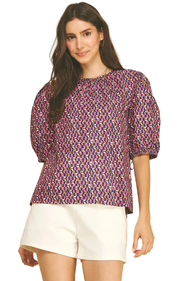 A model wearing the Geometric Print Puff Sleeve Blouse in navy and pink by PINCH, paired with white shorts, from Chatsworth Boutique in Fairhope, Alabama.