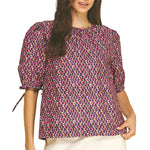 A model modeling the navy and pink geometric print puff sleeve blouse by PINCH with self-tie cuff detail, paired with white shorts, from Chatsworth Boutique.