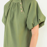 A model posing in the Olive Gold Button Blouse by THML, a cotton-spandex woven blouse, from Chatsworth Boutique in Fairhope, Alabama.