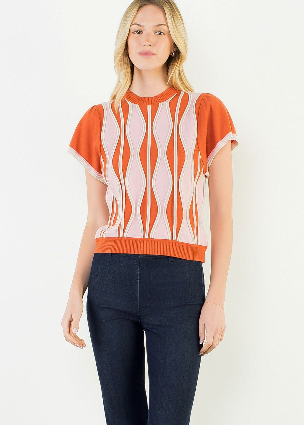A model wearing the Orange Ruffle Knit Blouse by THML, a wavy print knit top in orange, pink, and white, from Chatsworth Boutique in Fairhope, Alabama.
