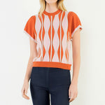 A model wearing the Orange Ruffle Knit Blouse by THML, a wavy print knit top in orange, pink, and white, from Chatsworth Boutique in Fairhope, Alabama.