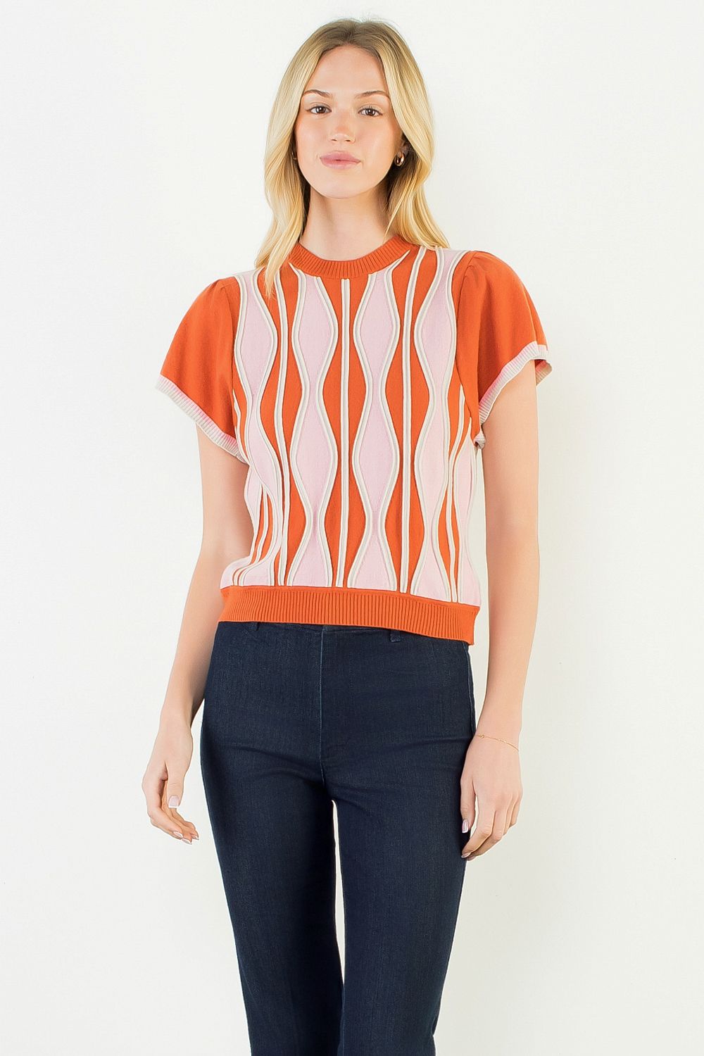 A model wearing the Orange Ruffle Knit Blouse by THML, a wavy print knit top in orange, pink, and white, from Chatsworth Boutique in Fairhope, Alabama.