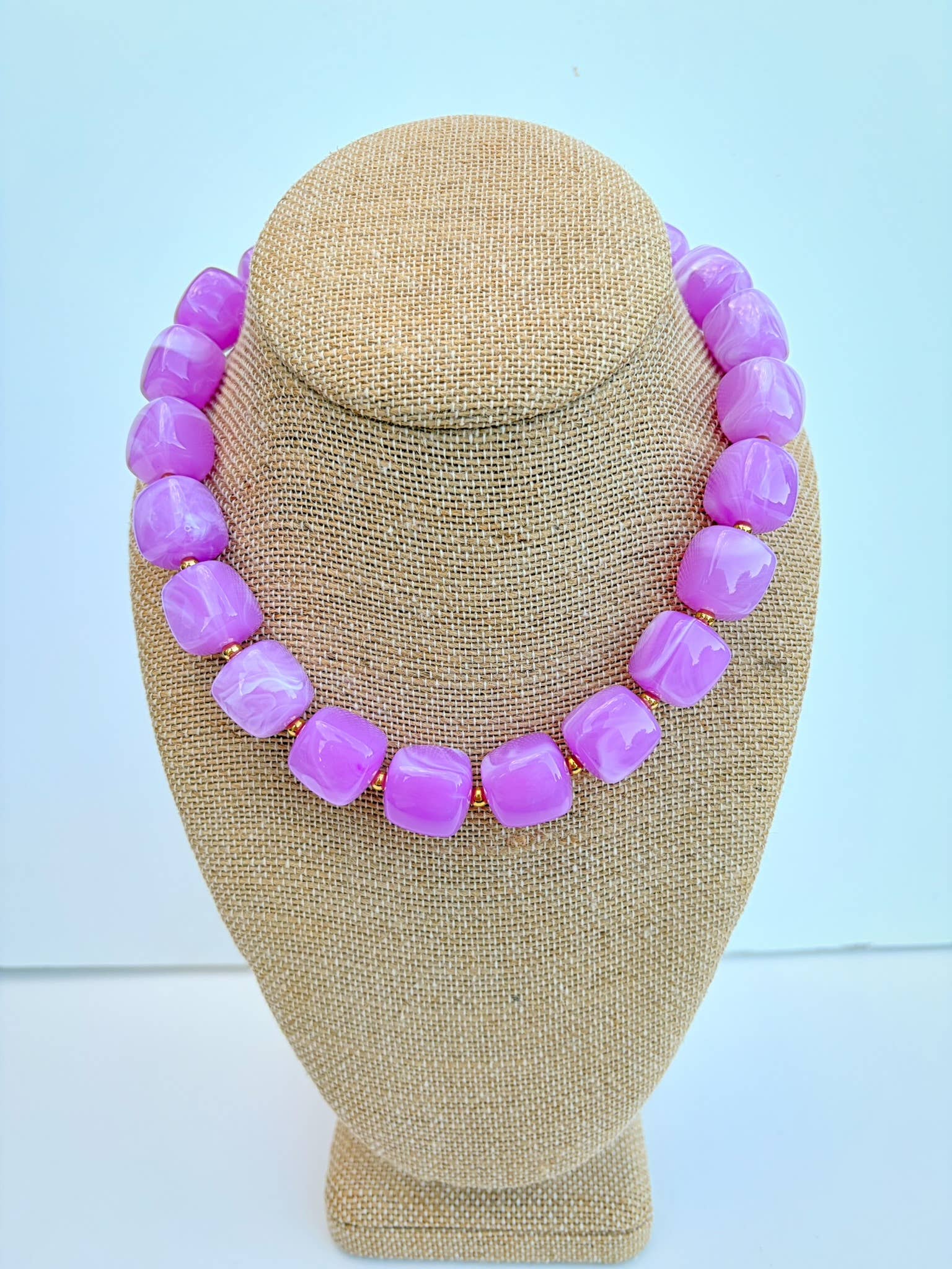 Necklace with purple beads on a beige mannequin bust against a light blue background