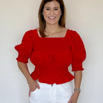A model wearing the Ruby Top in red by LaRoque, a peplum-style top with ruffle hem detail, from Chatsworth Boutique in Fairhope, Alabama.