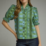 A model wearing the Stripes and Dots Blouse in green by Entro, a mixed print top with a ruffle neckline and puff sleeves, from Chatsworth Boutique in Fairhope, Alabama.
