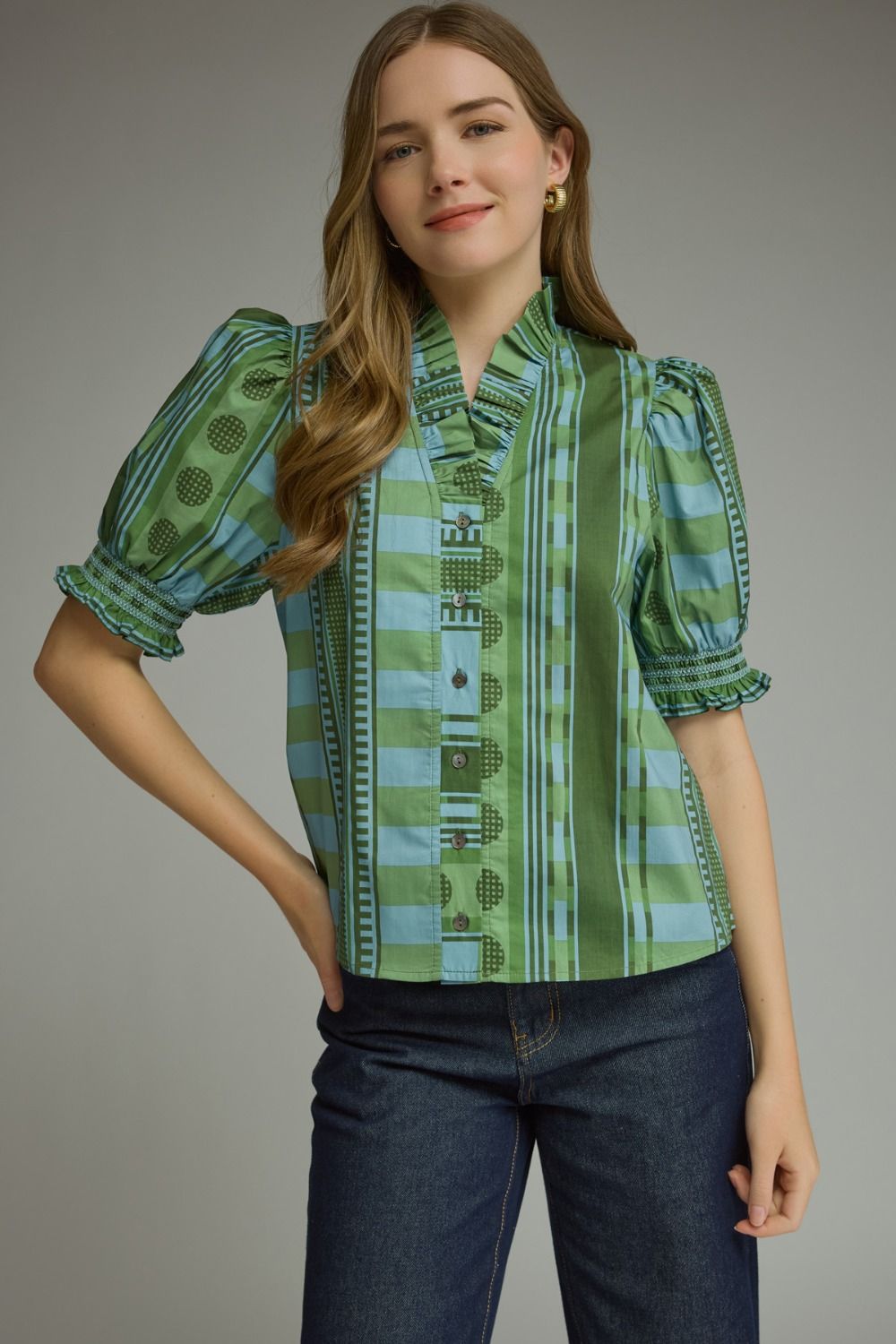 A model wearing the Stripes and Dots Blouse in green by Entro, a mixed print top with a ruffle neckline and puff sleeves, from Chatsworth Boutique in Fairhope, Alabama.