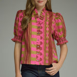 A model wearing the Stripes and Dots Blouse in pink and chartreuse by Entro, a mixed print top with a ruffle neckline and puff sleeves, from Chatsworth Boutique in Fairhope, Alabama.
